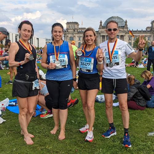Four runners with finisher medals on the lawn in front of the Reichstag in Berlin