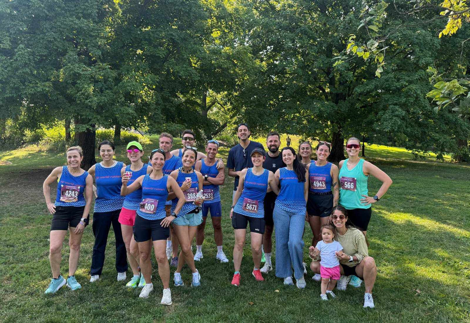 NY World Runners team members in race bibs and blue team singlets, smiling together in the park